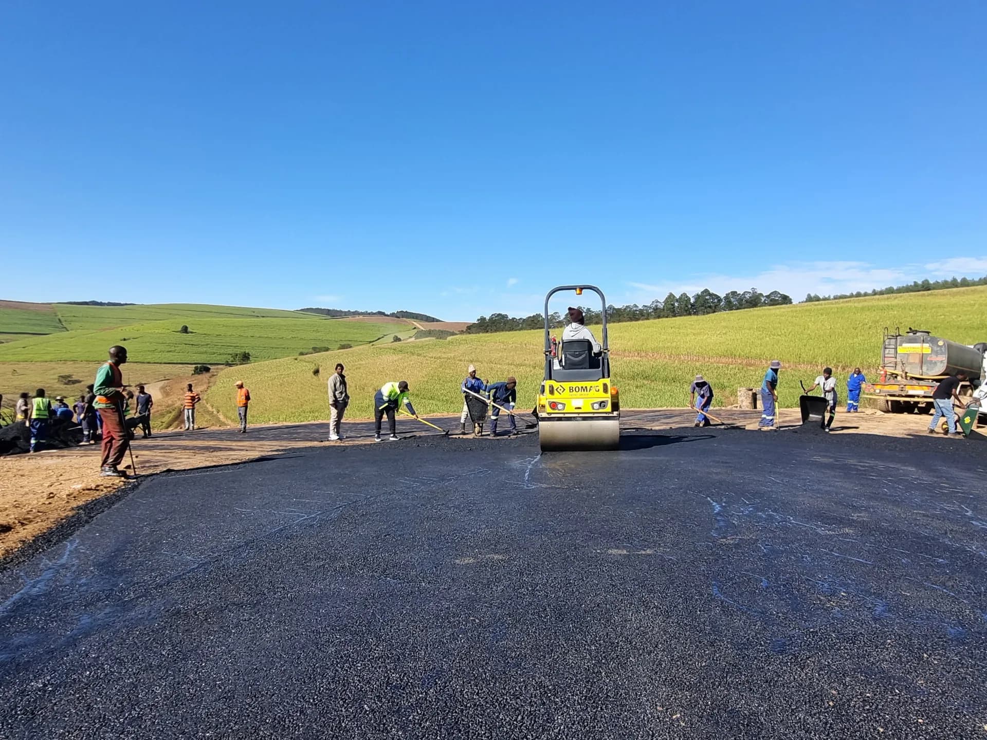 Crew laying asphalt on a rural access road with a roller behind